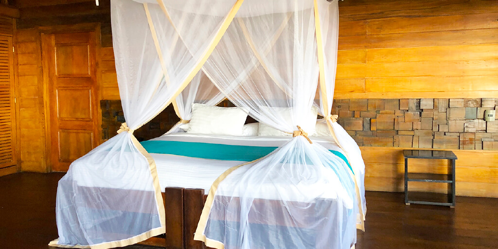 Habitación con cama doble, toldillo y paredes de madera