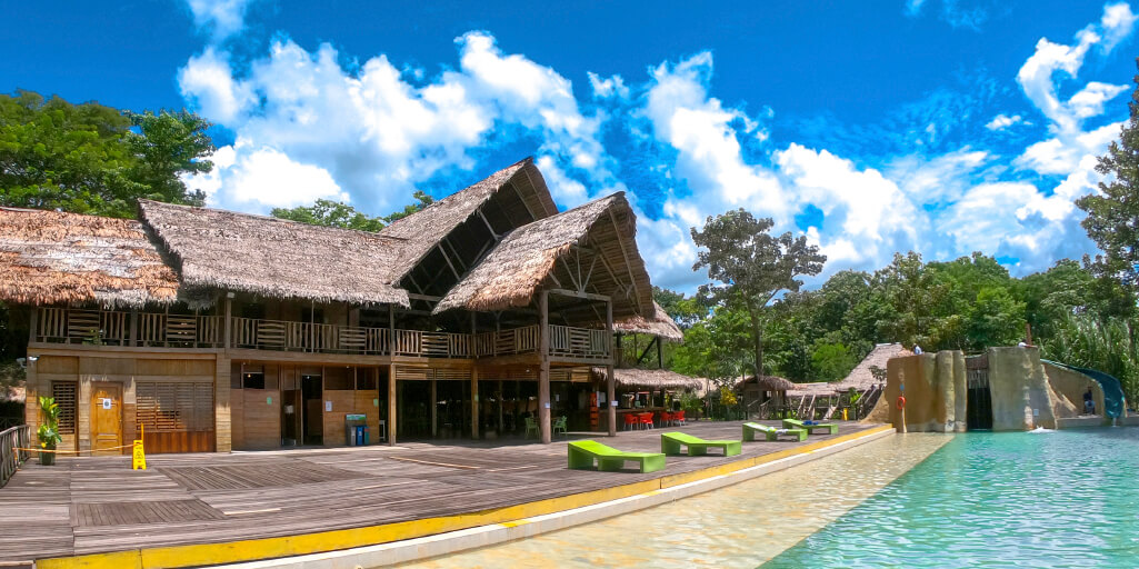 El edificio principal del hotel, con techo de palma, visto desde la piscina y el tobogán